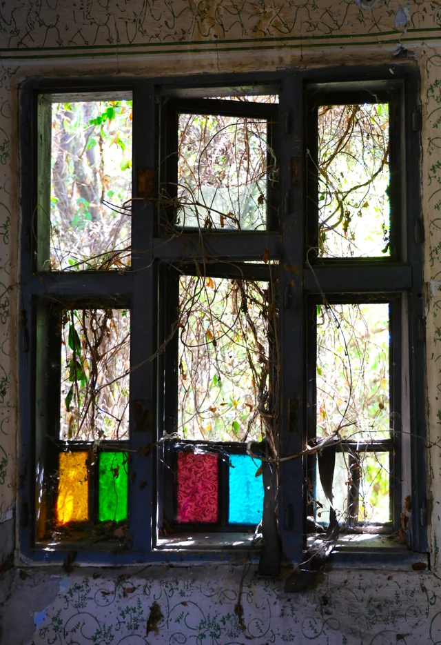 Small colored panes remain in the window of a dark abandoned room.