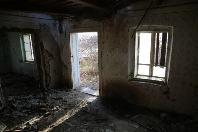 An open doorway and windows illuminate a dark, debris-filled room.