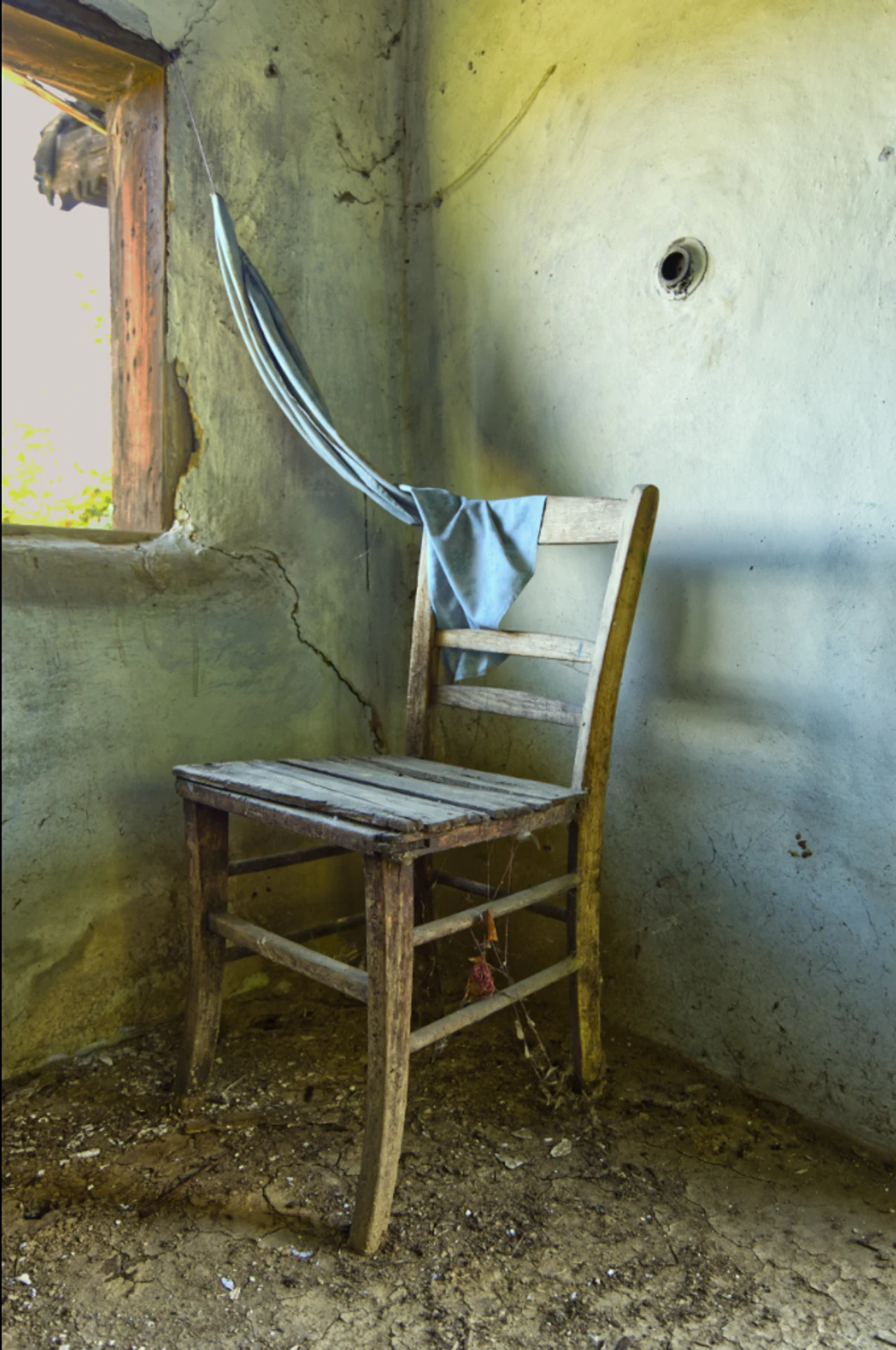 A wooden chair beside a window in an abandoned room.