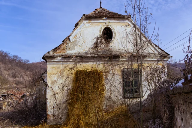 An abandoned chapel with a round window and overgrown entrance.