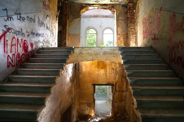A split staircase in a ruined building, lit through arched windows.